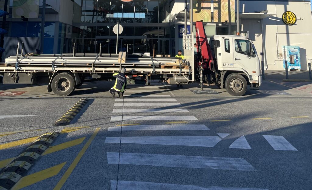 A photo of an entry to a mall. There is a large truck parked across all of the disabled parking bays and pedestrian crossing. 